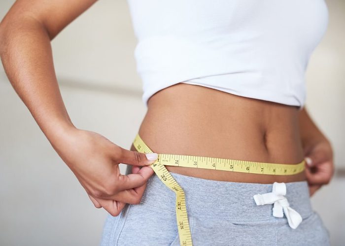 Cropped shot of a young woman measuring her waist in the bathroom