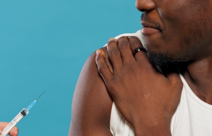 Hands of doctor preparing to vaccinate young man against coronavirus